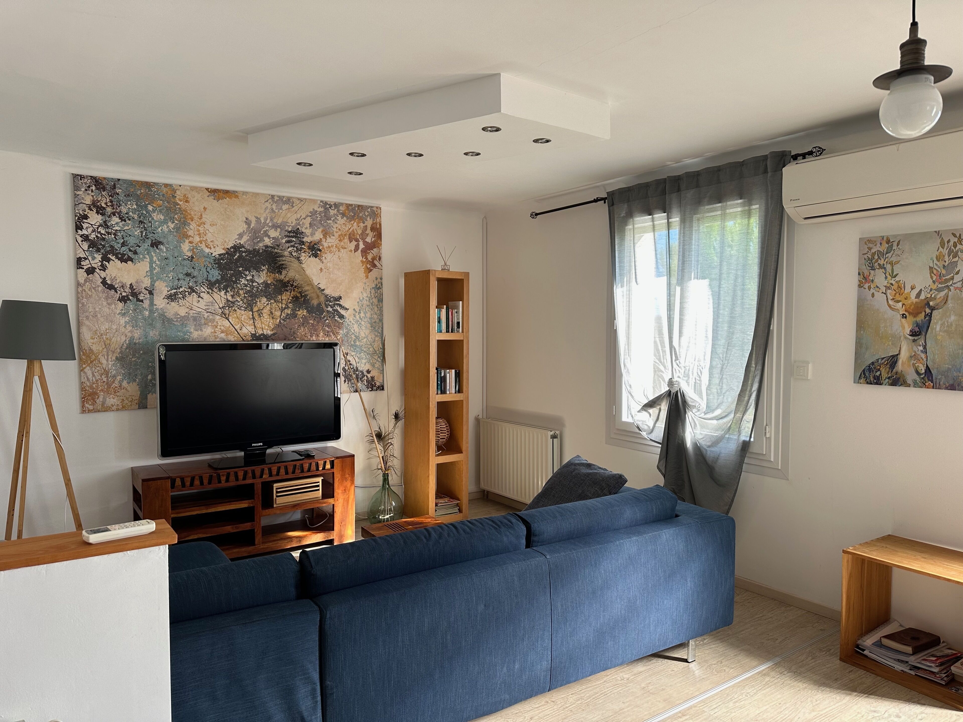 Un salon avec un grand canapé bleu, un téléviseur à écran plat posé sur un meuble en bois, une bibliothèque et un tableau accroché au mur.