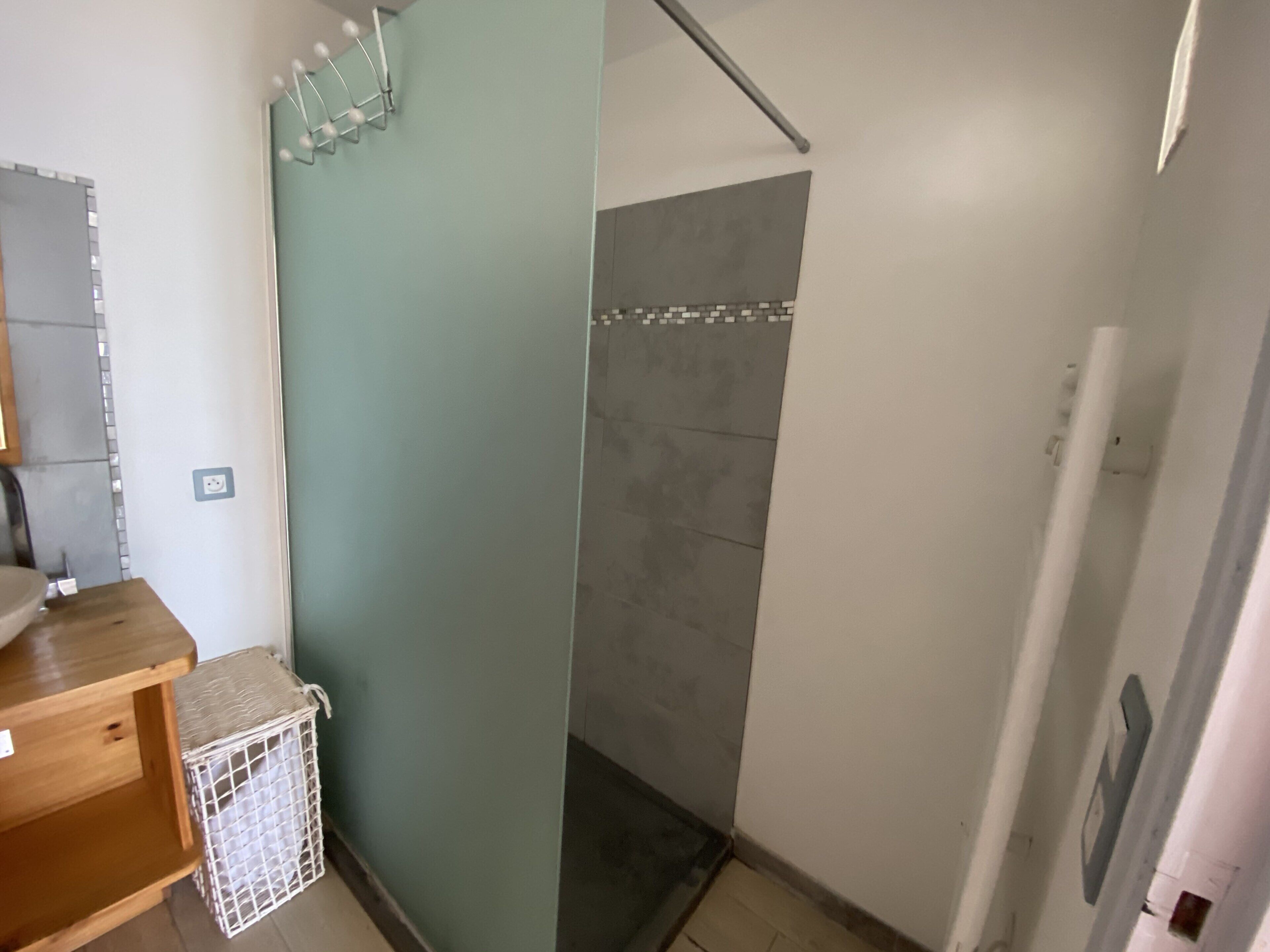 Un bagno con doccia, una panca in legno e un cesto per la biancheria bianco.