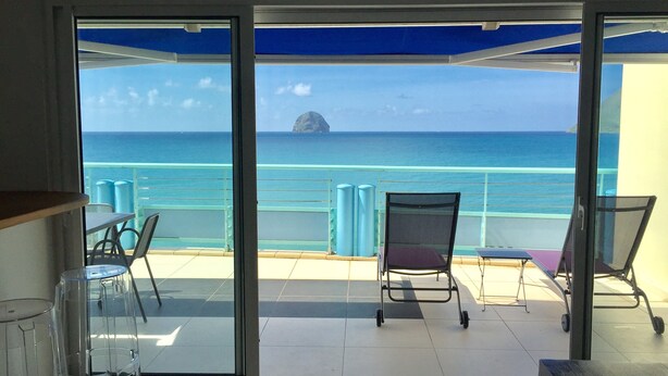 Un balcone con vista libera sull'oceano e un'isola in lontananza. Sul balcone ci sono due sedie e un tavolo.