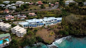 Vista aerea di un resort costiero con diversi edifici, una spiaggia e una piscina.