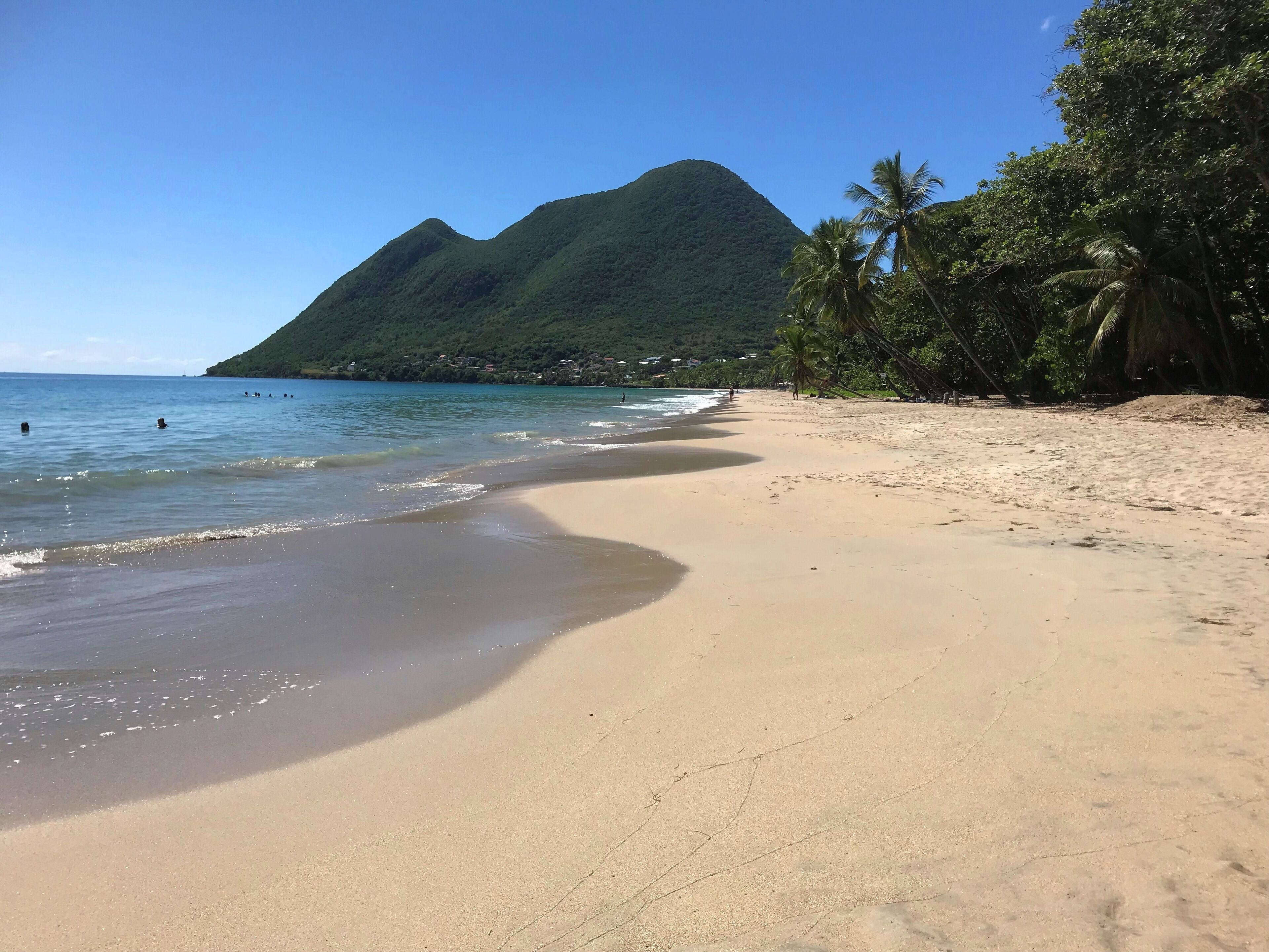 Una playa con agua cristalina, una orilla arenosa y una montaña al fondo.
