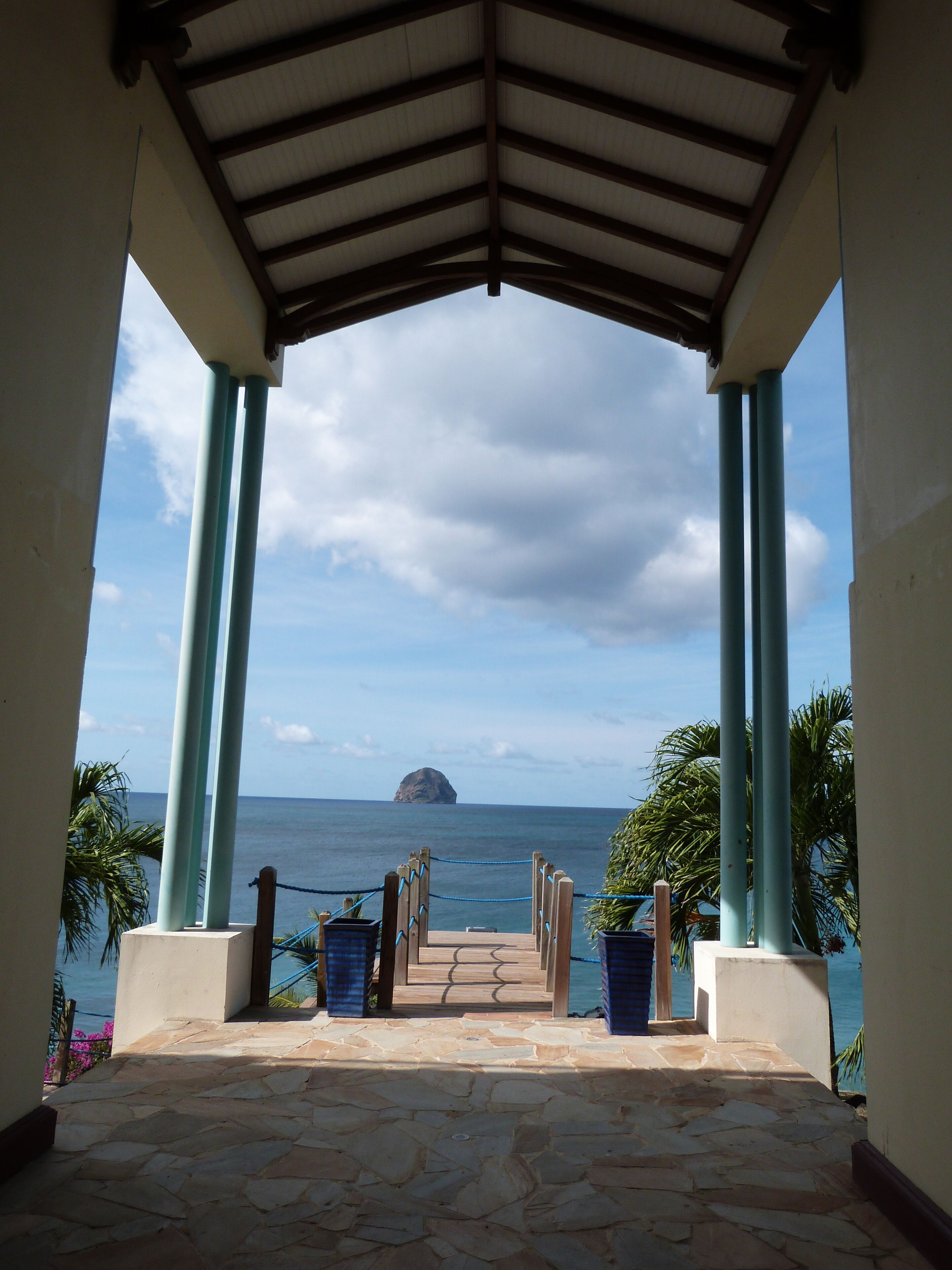 A stone-paved pathway leading to a beach view under a covered structure with columns.