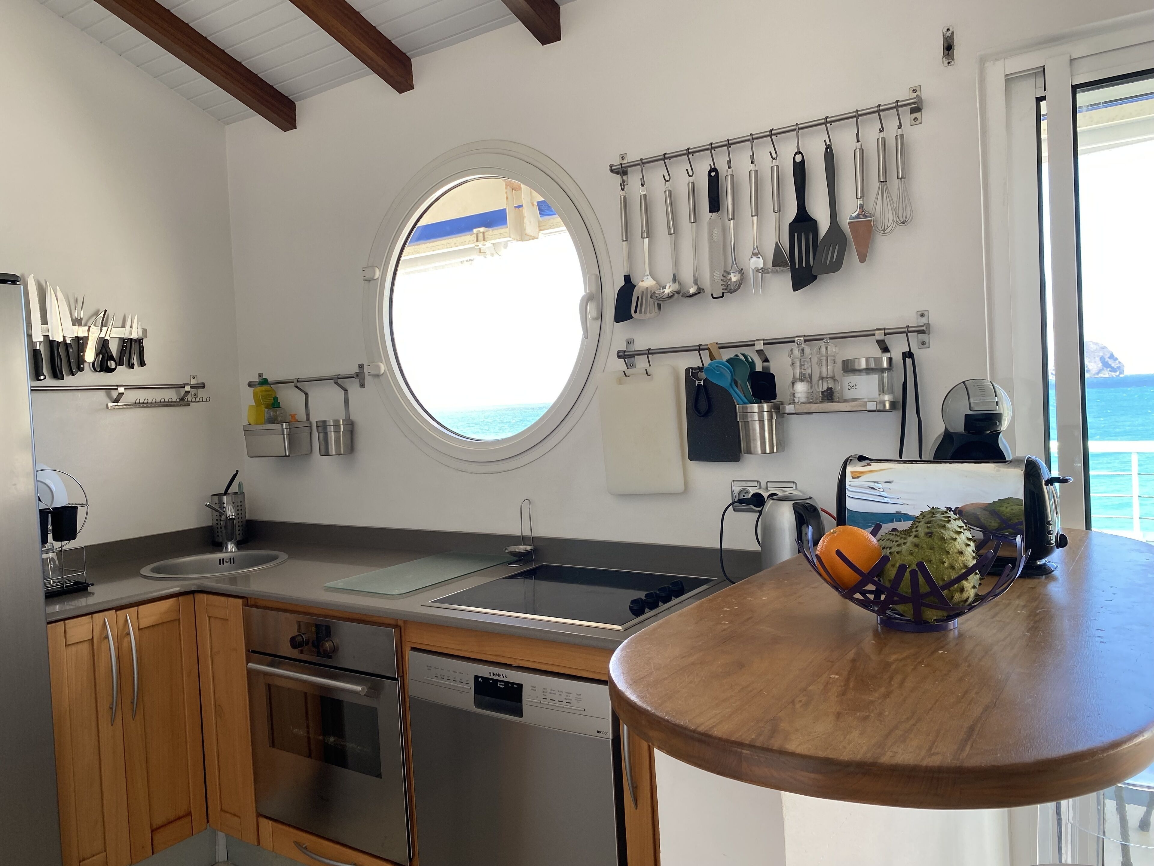 Una cocina moderna con electrodomésticos de acero inoxidable, un ventanal redondo y vistas al mar.