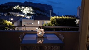Un balcón con una mesa y sillas, un farol decorativo, y vistas del Hotel Le Golfe con montañas al fondo.