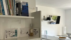 Una cocina moderna con armarios blancos, un televisor de pantalla plana montado en la pared y una encimera con un bol y una taza de café.