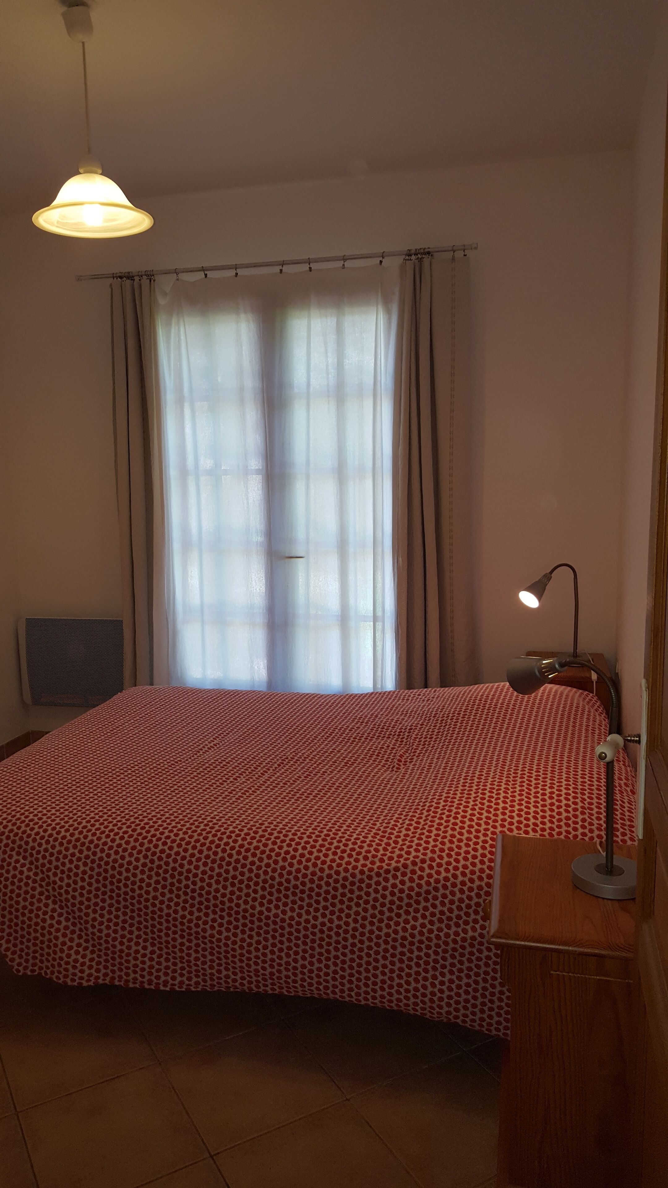 Una camera da letto con un letto, una scrivania, una lampada, una finestra con tende e un lampadario.
