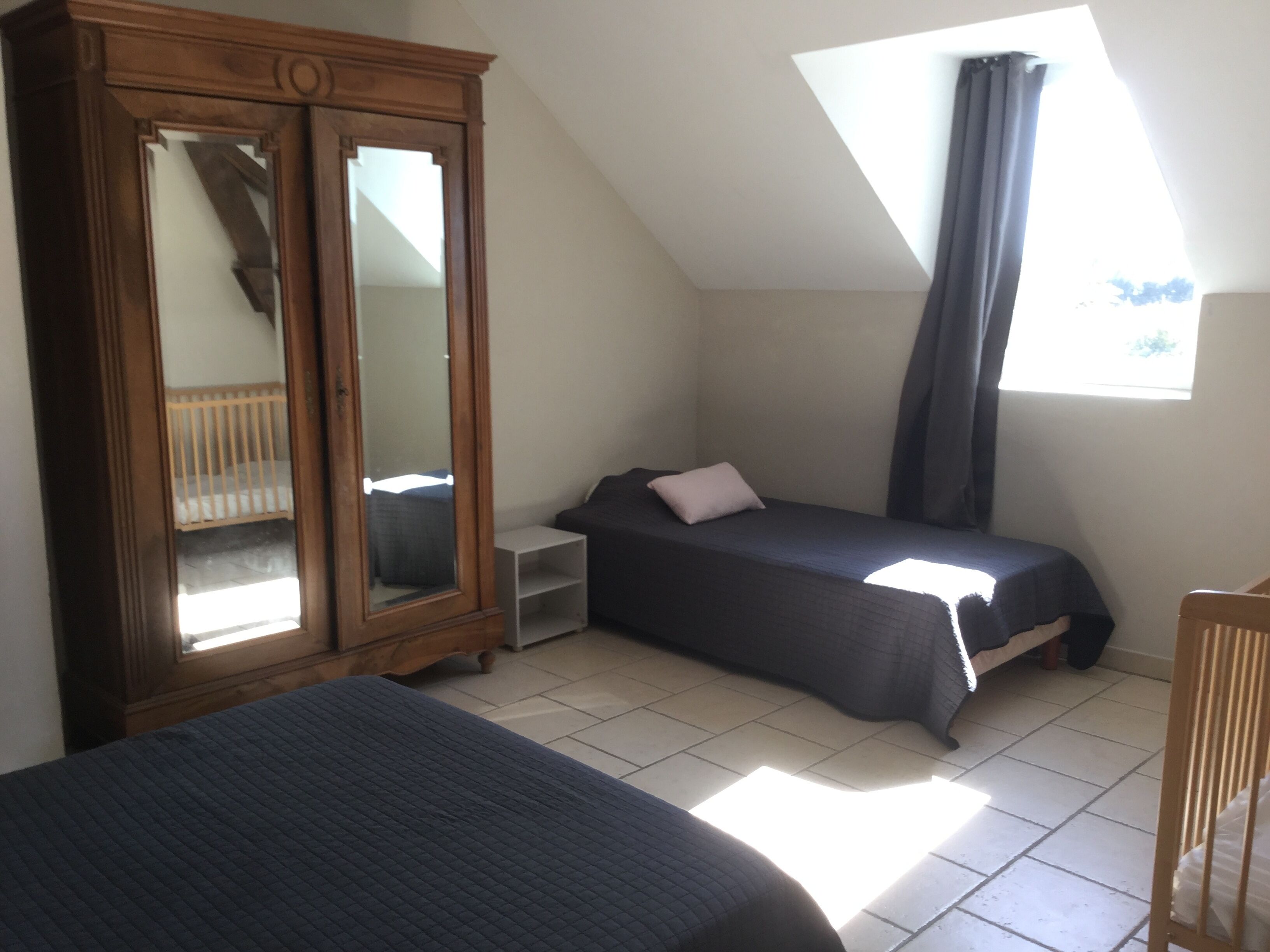Un dormitorio con cama, armario, mesita de noche, ventana con cortinas y un tragaluz.