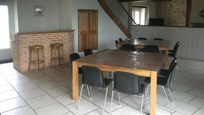 Een ruime eethoek met een grote houten tafel en zwarte stoelen, een accentmuur van baksteen en een trap naar een verdieping erboven.