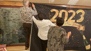 Drie personen werken aan een groot zwart decor met de tekst '2023 New Year' en een afbeelding van een champagnefles.
