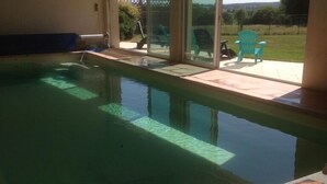 Een binnenzwembad met glazen wanden, een terrasgedeelte met stoelen en uitzicht op de omgeving.