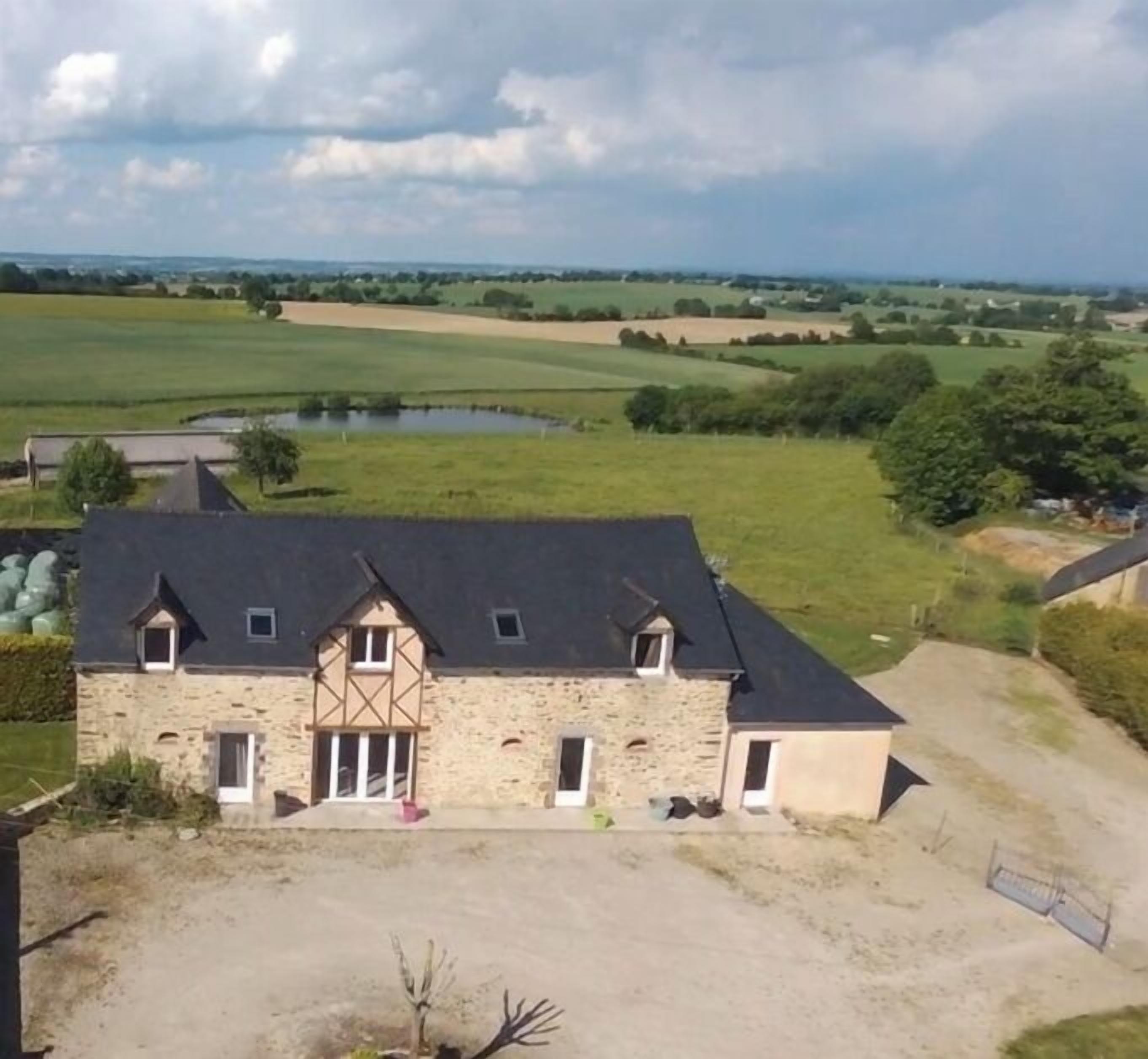 Un bâtiment en pierre, doté d’un toit sombre, entouré de champs ouverts et d’un étang.