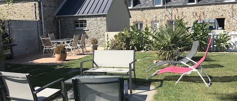 A stone building with a sloped roof, outdoor seating with chairs and a table, and a grassy lawn.
