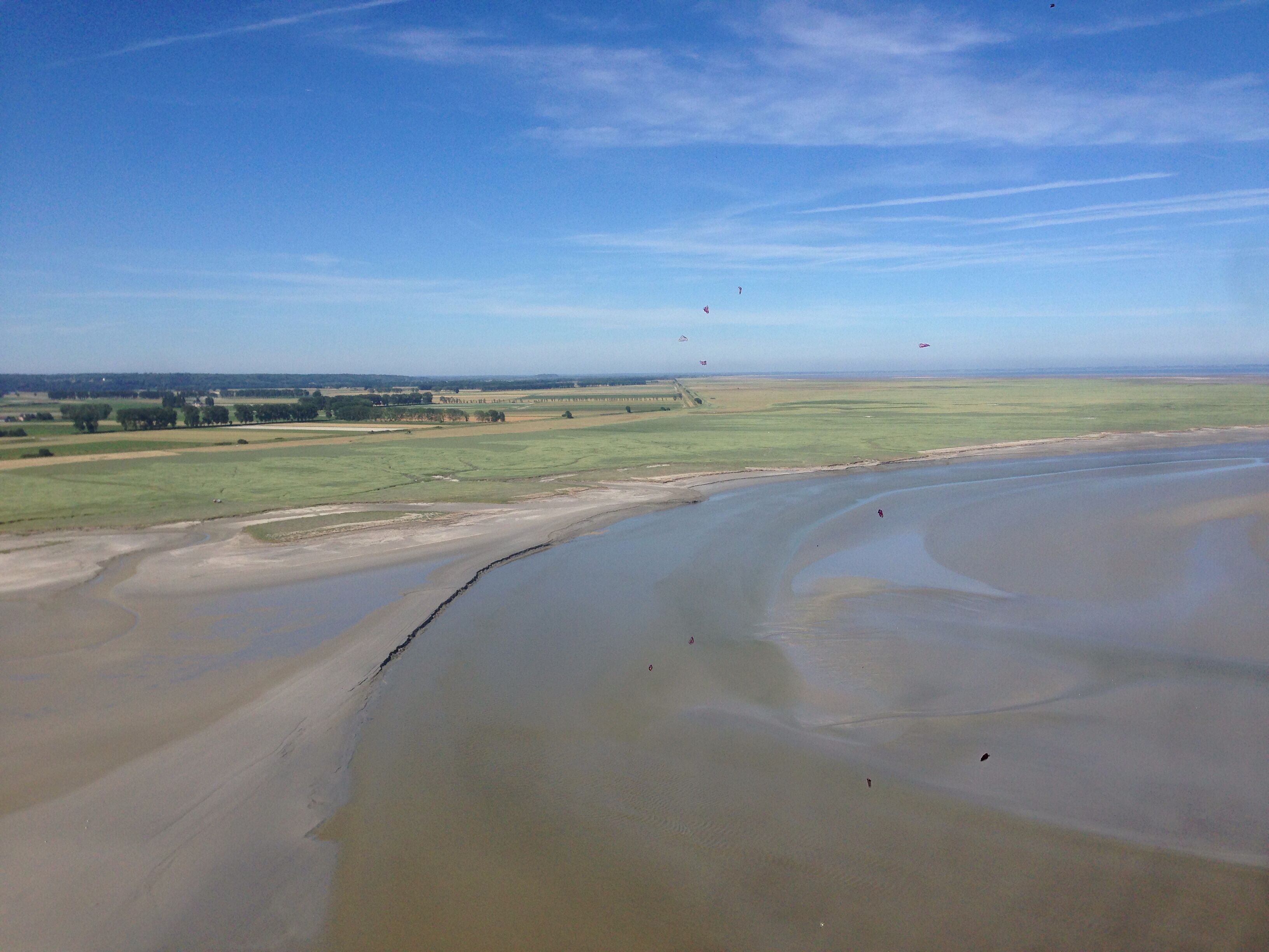 Una orilla de río amplia con una playa arenosa y un campo de hierba a lo lejos.