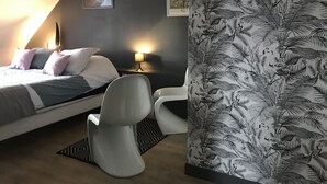 A bedroom with a bed, two chairs, a nightstand, a lamp, and a wall with a tropical wallpaper. - *** house in Mont Saint Michel bay for 2 to 5 people (Saint-Broladre)