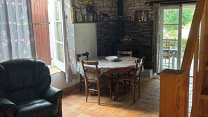 A rustic room with a stone wall, a wooden table with chairs, a black leather armchair, and a wooden staircase. - Private garden, swimming pool, picturesque village location, bank, bakery (saint fort sur gironde)