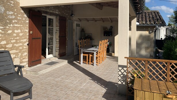 A covered outdoor patio with a table and chairs, a wooden bench, and a wooden fence. - Private garden, swimming pool, picturesque village location, bank, bakery (saint fort sur gironde)