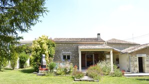 A stone building with a tiled roof, a covered porch, and a well-maintained garden with various plants and flowers. - Private garden, swimming pool, picturesque village location, bank, bakery (saint fort sur gironde)
