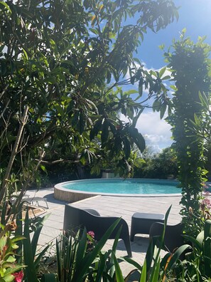 Relax by the serene pool surrounded by lush greenery and trees, with comfortable lounge chairs for unwinding.