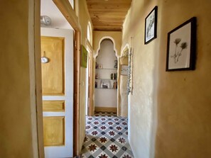 Stylish hallway with a door to a room, featuring a geometric patterned floor, framed artwork, and a wooden ceiling with exposed beams.