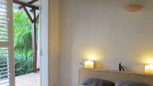 Ein Schlafzimmer mit einem Bett, zwei Nachttischlampen und Blick auf Grün hinter einer offenen Tür.