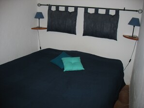 A bed with a dark blue bedspread and two teal pillows. There are two wall-mounted lamps on either side of the bed.