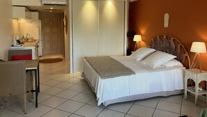 A hotel room with a bed, bedside tables, a desk with a chair, a kitchenette, and a bathroom. - BEAUTIFUL STUDIO NEAR THE BEACH IN THE HEART OF THE ORIENT BAY VILLAGE (Orient Baie)