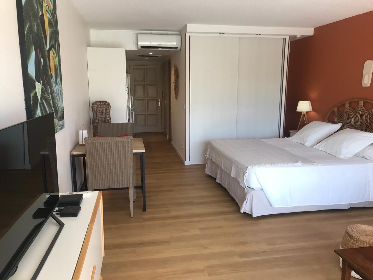 A hotel room with a bed, a desk, a chair, a TV, and an air conditioning unit.