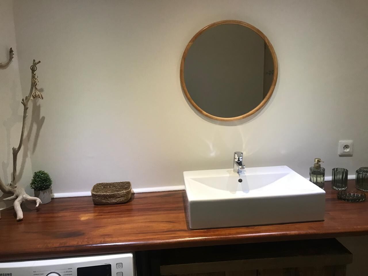 Een badkamer met een wit wastafel, een ronde spiegel en een houten aanrechtblad.