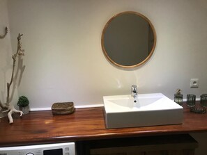 A bathroom with a white sink, a round mirror, and a wooden countertop.
