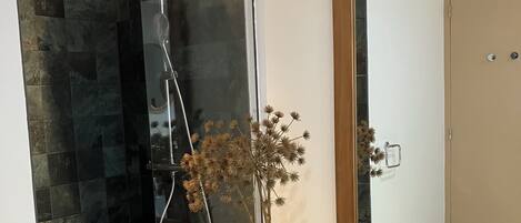 A modern bathroom with a glass-enclosed shower, a large mirror, and a vase with dried flowers.