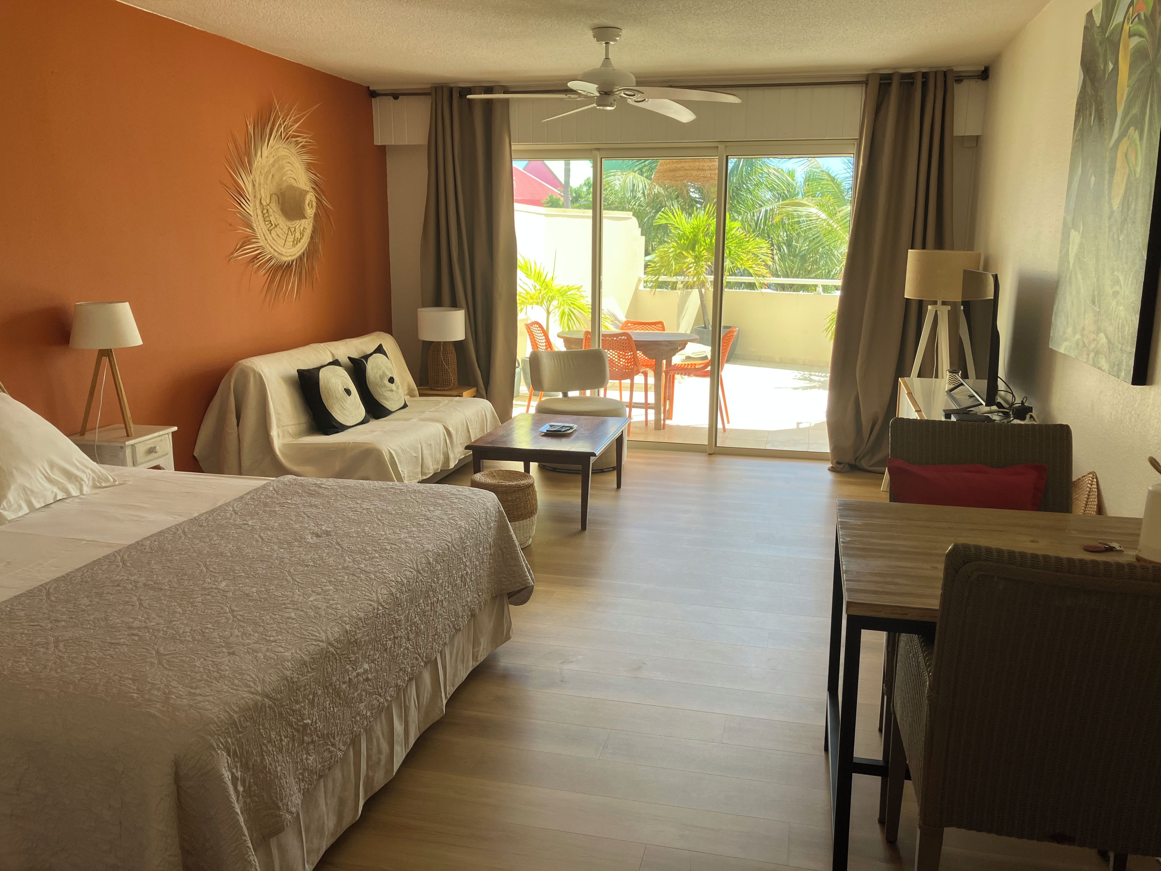 A hotel room with two beds, a sofa, a dining table, and a balcony with outdoor furniture.