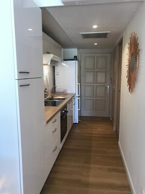 A narrow hallway with a kitchen area on one side, featuring cabinets, a sink, and a stove. - BEAUTIFUL STUDIO NEAR THE BEACH IN THE HEART OF THE ORIENT BAY VILLAGE (Orient Baie)