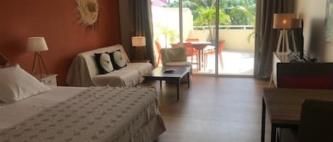 A hotel room with two beds, a sofa, a table, and a balcony with outdoor seating.