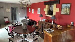 A dining area with a round table, chairs, a chandelier, and a red wall with artwork. - Quiet, dead-end street, 10 minutes' walk from the town center, ground floor (Sarlat-La-Canéda)