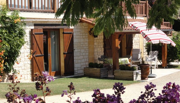 A stone building with wooden shutters, outdoor seating, and a striped umbrella. - Quiet, dead-end street, 10 minutes' walk from the town center, ground floor (Sarlat-La-Canéda)