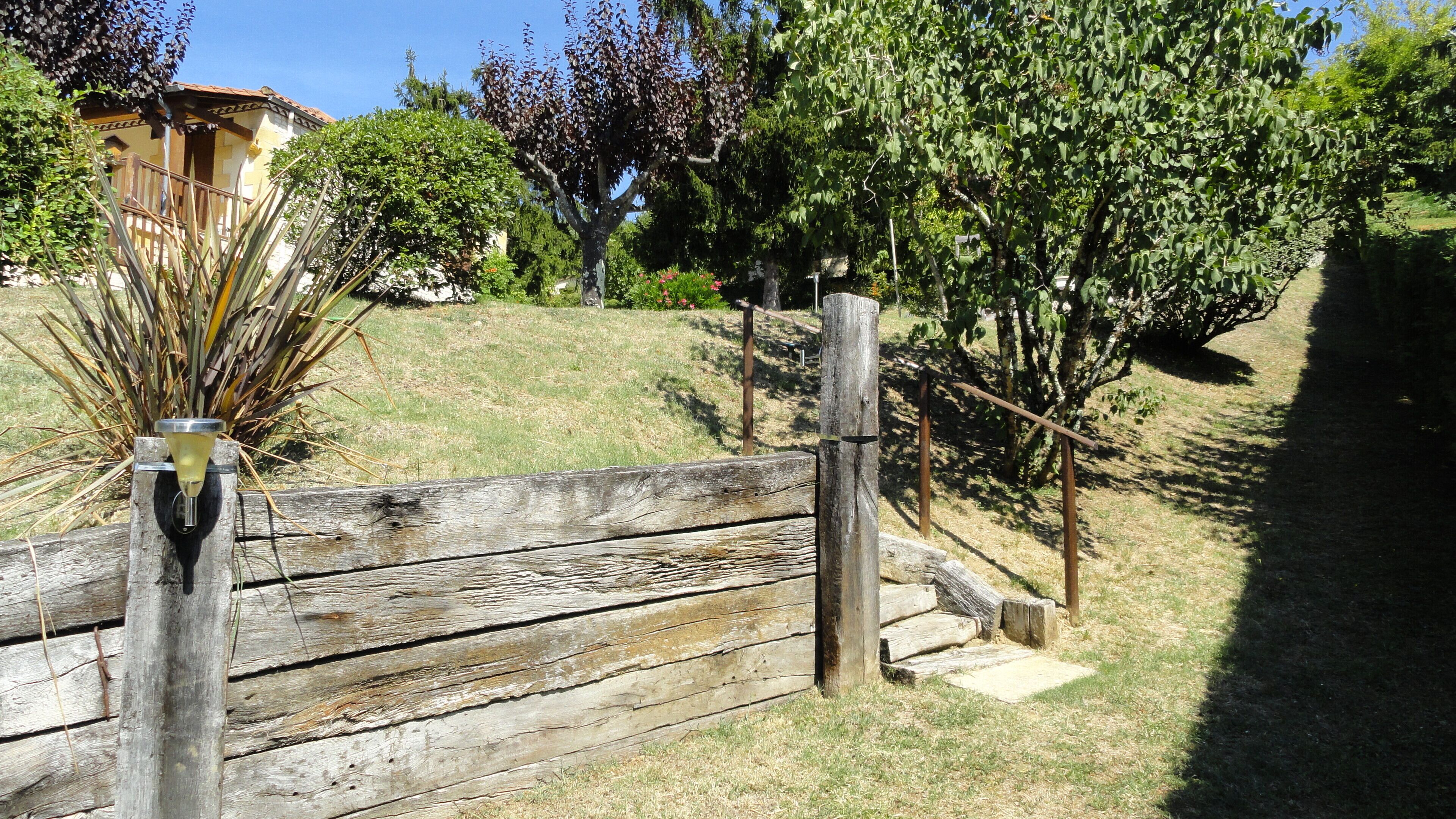 A wooden gate leading to a grassy area with a fountain and trees.