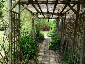 A wooden pergola with a concrete pathway leading through a garden. - Rental of a mill in the countryside in a beautiful green setting (La Selve)