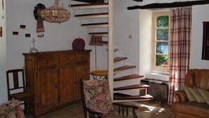 Une pièce avec un escalier en bois, une armoire en bois, un fauteuil à motifs floraux, un canapé en cuir marron et une fenêtre avec des rideaux.