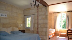 A bedroom with a bed, a bench, a chair, a window with curtains, a chandelier, and a stone wall with a nameplate. - House with character, Gardegan-et-Tourtirac (Gardegan-Et-Tourtirac)