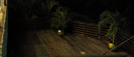 Una piscina con agua cristalina, rodeada por una terraza de madera y plantas en macetas.