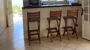 Una cocina con barra, dos sillas de madera, un refrigerador y una ventana con persianas.
