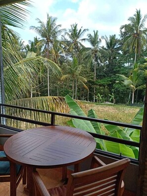 A balcony with a round wooden table and chairs, overlooking a rice field and palm trees. - Semanggi Cottage (Ubud)