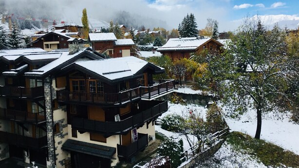 Een besneeuwd bergdorp met traditionele houten gebouwen, balkons en een heldere lucht.