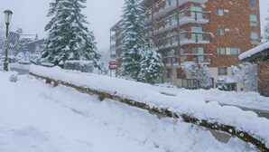 Een meerlaags gebouw met balkons, omringd door met sneeuw bedekte bomen en een besneeuwde straat.