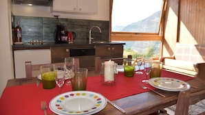 Een eettafel gedekt met borden, glazen en een kaars als middelpunt, met uitzicht op een berg door een raam.