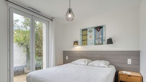 Un dormitorio con cama, mesita de noche, lámpara de pared, un cuadro y una puerta corrediza de vidrio que da a un espacio exterior.