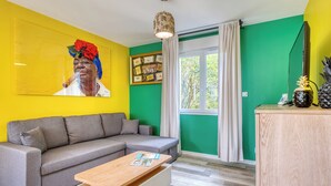 Una sala de estar con un sofá gris, una mesa de centro de madera, un cuadro en la pared, una ventana con cortinas y un mueble de madera con un adorno de piña.