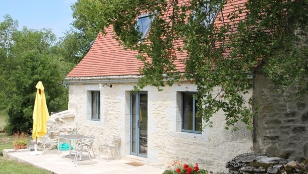 Ein Steinhäuschen mit rotem Ziegeldach, einer Terrasse mit Gartenmöbeln und Blumentöpfen.