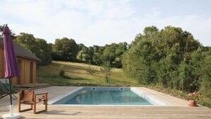 Eine Holzterrasse mit Swimmingpool, einer Holzhütte und einem Stuhl mit violettem Sonnenschirm.