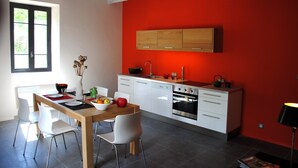 A modern kitchen with white cabinets, a red accent wall, and a wooden dining table with chairs. - South Ardèche in Balazuc, listed site, Les Faysses self-catering gîte with charm and character (Balazuc)